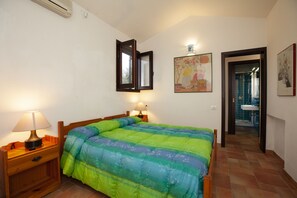 A bedroom with a bed, bedside lamps, a wall-mounted mirror, and a bathroom visible through an open door.