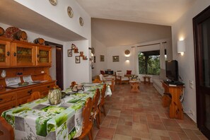 A dining area with a long table, chairs, and a television on a stand.