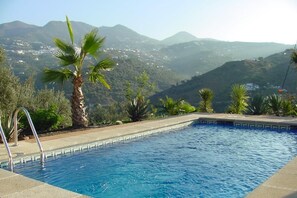 A swimming pool with a view of mountains, surrounded by palm trees and a clear sky.