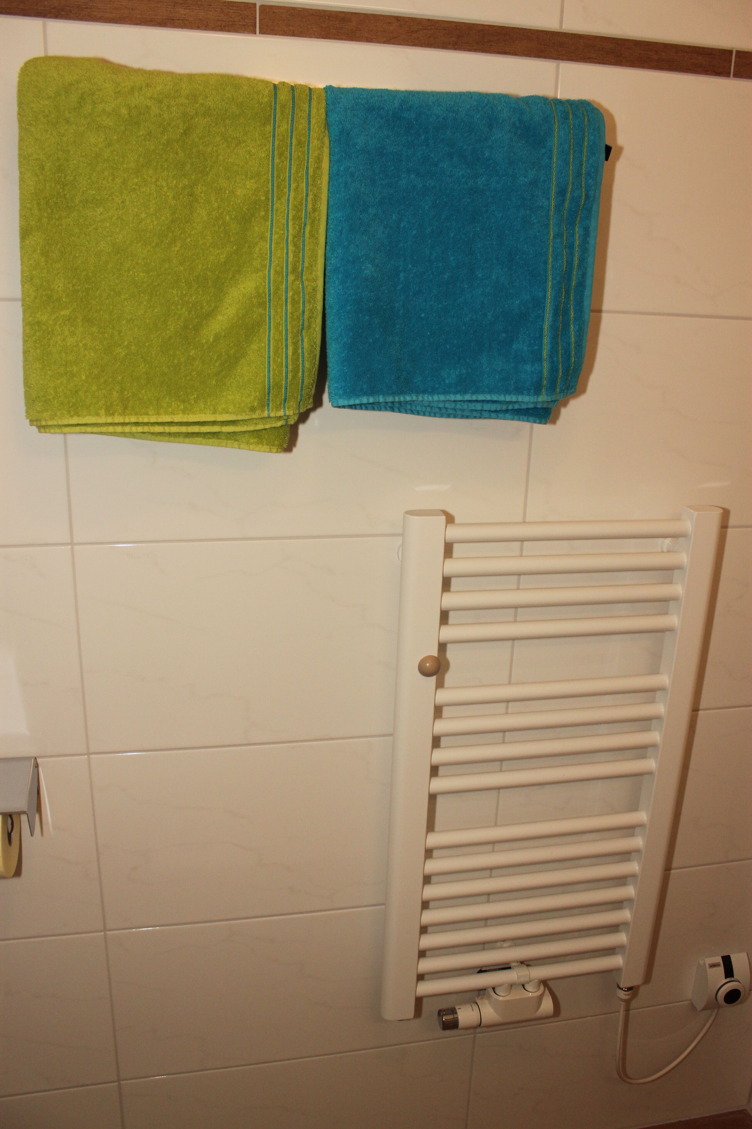 A bathroom with a white radiator, a green and a blue towel hanging on the wall.