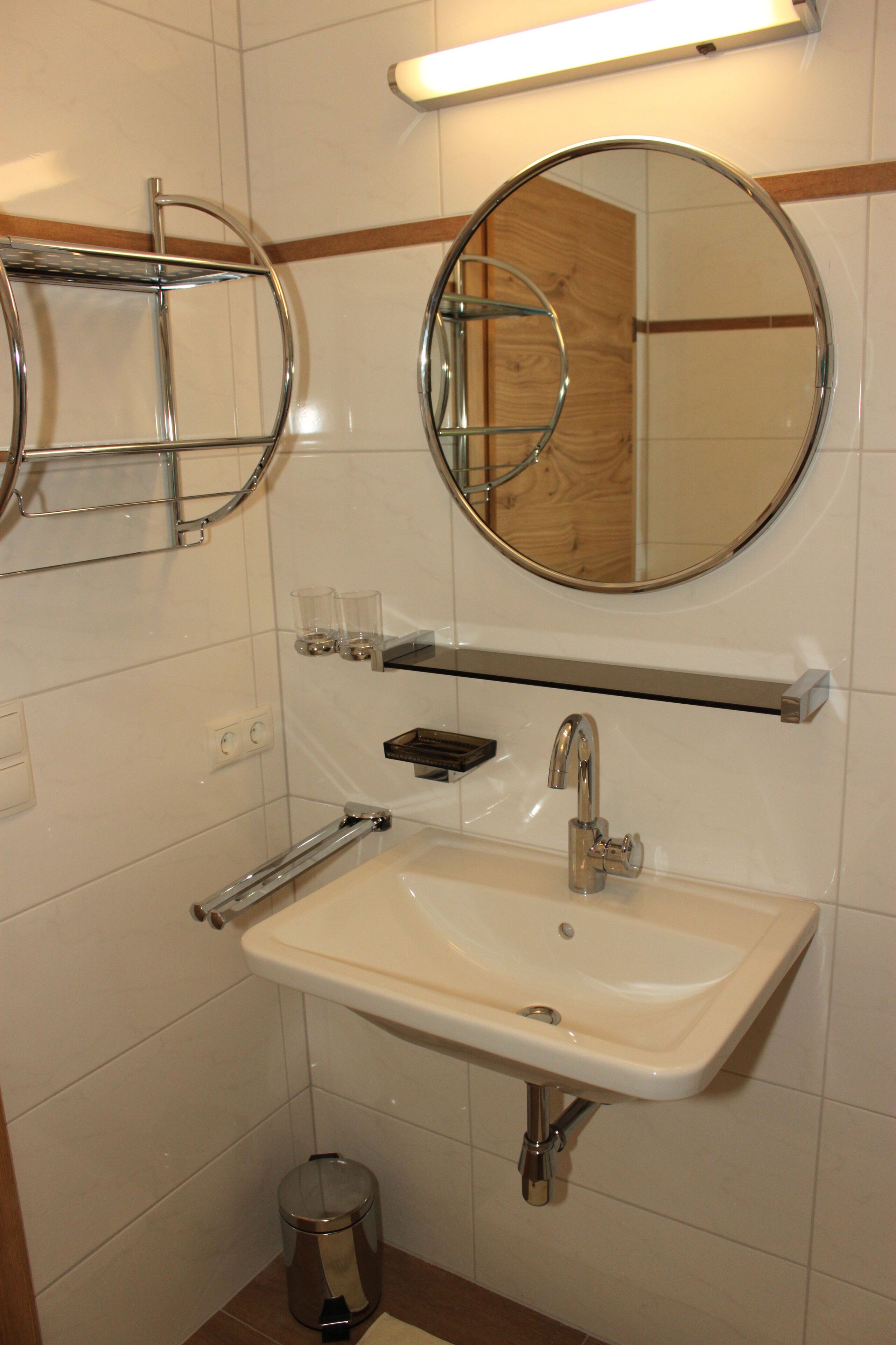 A bathroom with a white sink, chrome fixtures, a mirror, and a small trash can.