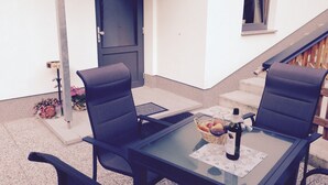 Ein Außenbereich mit Sitzgelegenheit, zwei Stühlen, einem Tisch, einer Tür, einem Fenster und einer Treppe.