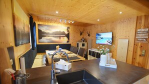 Un intérieur en bois comprenant un coin repas, une cuisine avec un évier, un téléviseur et des éléments de décoration fixés au mur.