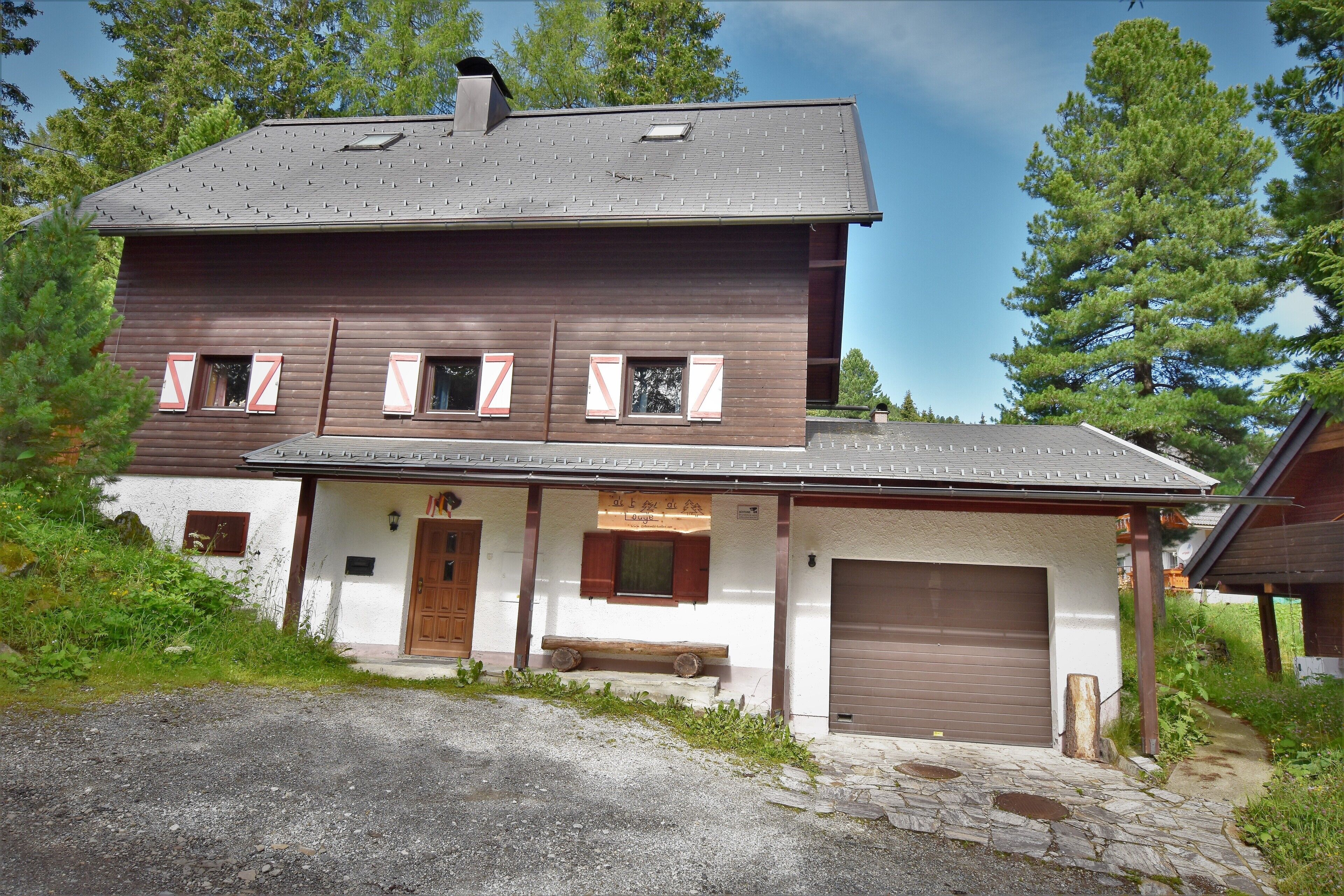 Une maison en bois à deux étages, avec un garage, un banc à l’extérieur et une allée gravillonnée.