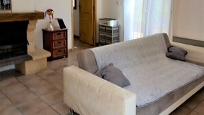A living room with a sofa, a fireplace, a chandelier, and a door leading to another room. - On the edge of a forest, in green Provence, with private swimming pool (Brignoles)