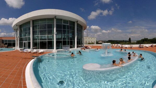 Zona de piscina con un edificio moderno, sillas de descanso y cielo despejado.