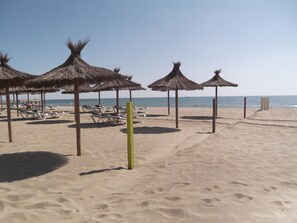 Una playa con sombrillas de paja y sillas reclinables blancas.