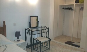 Un dormitorio con cama, mesita de noche con lámpara, silla, armario y zona de ducha.