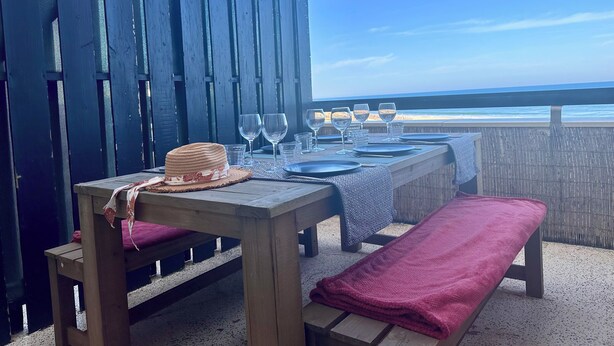 A wooden table set for dining with a view of the ocean, a wooden bench with a red cushion, and a straw hat on the table. - Magnificent 60m² apartment - 6 people with ocean view terrace South Beach  (Lacanau)
