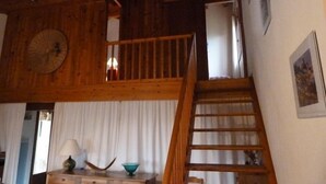 Interior rústico de madeira com área de dormir no mezanino, escada e vista para o exterior.