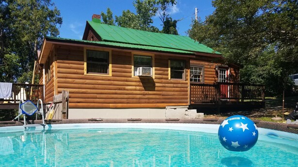 En træhytte med grønt tag, en swimmingpool og en blå bold med stjerner.