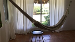 Una hamaca en una habitación con vistas a un jardín a través de una ventana con cortinas blancas.