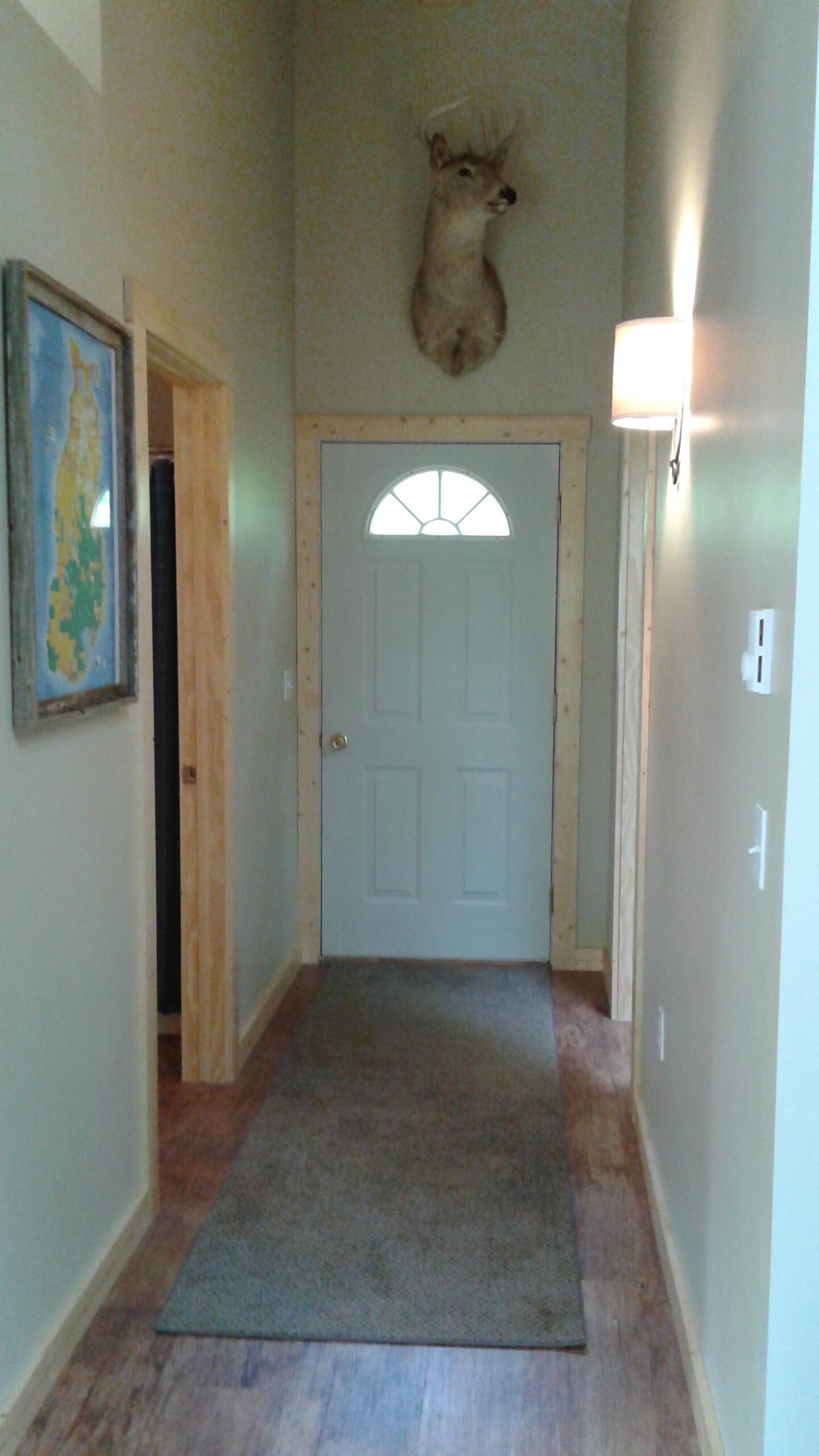 A hallway with a wooden door, a mounted deer head, a framed map, and a light fixture.