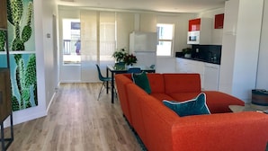 A modern living space with a bright kitchen, a dining area with a table and chairs, and a large orange sofa. - Steps to sand! Ocean view, Walk to village, family friendly, A/C! (Carlsbad)