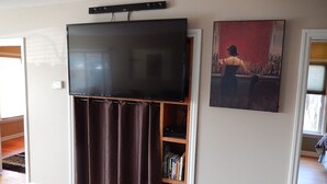 Ein Wohnzimmer mit einem an der Wand befestigten Flachbildfernseher, einer Bücherwand mit Büchern und einem gerahmten Bild.