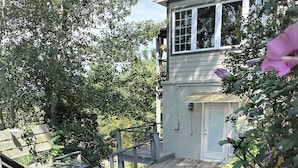 A wooden deck leading to a house with a covered porch, surrounded by lush greenery and flowering plants. - King en suites.  Enjoy panoramic views of city and mountains, Walkable to town. (Asheville)