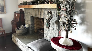 A cozy living room with a fireplace, a Christmas tree, and a television mounted on the wall. - King en suites.  Enjoy panoramic views of city and mountains, Walkable to town. (Asheville)