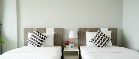 Habitación de hotel con dos camas, cada una con una almohada y una mesita de noche con una lámpara y un objeto decorativo pequeño.
