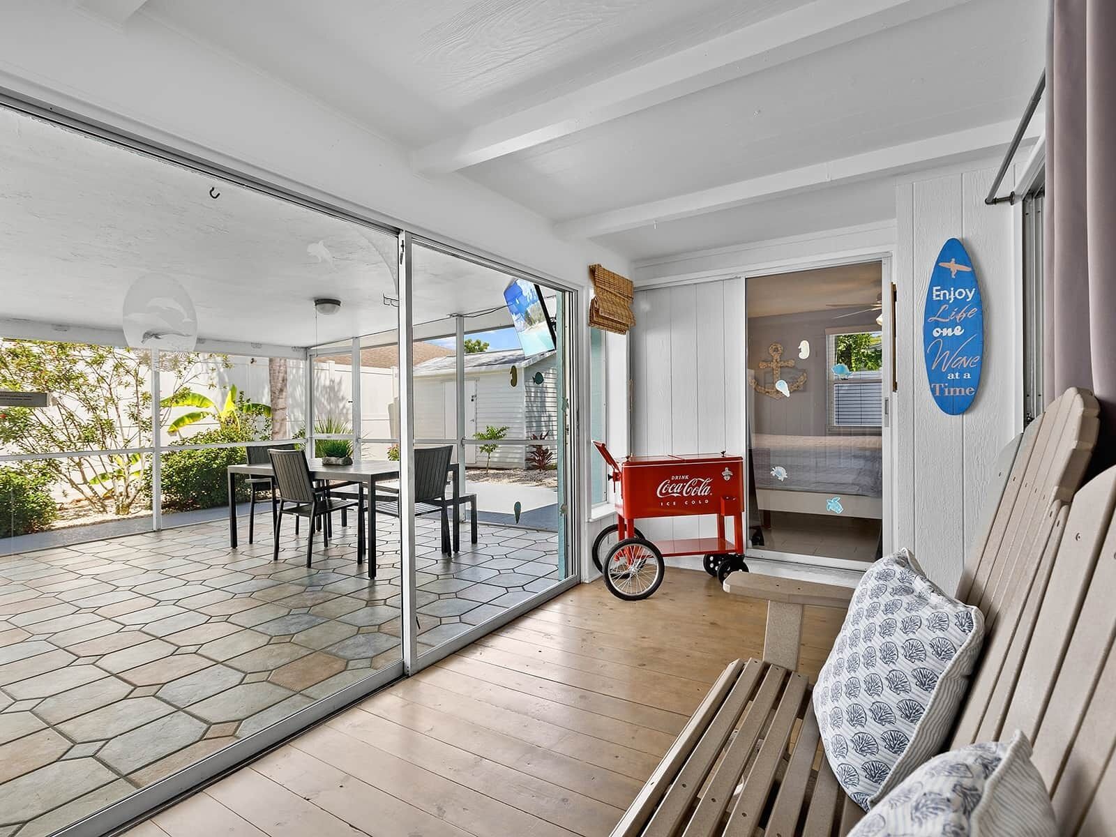 A room with a glass door leading to an outdoor area, a red Coca-Cola cooler, a bench with patterned cushions, and a wall with a blue sign.