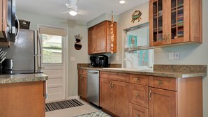 A kitchen with wooden cabinets, a stainless steel refrigerator, a coffee maker, and a dishwasher. - Tana’s Siesta Getaway - Heated Private Pool (Sarasota)