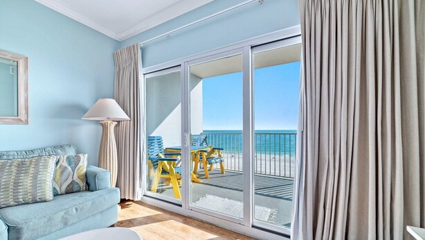 Una habitación con un sofá azul, una lámpara y vistas a la playa a través de un ventanal corredero.