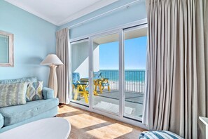 Une pièce avec un canapé bleu, une lampe et une vue sur la plage, visible à travers une porte-fenêtre coulissante.
