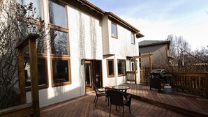 Une maison à deux étages dotée d’une terrasse, de grandes fenêtres et d’un barbecue.