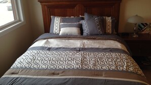 Un lit bien fait, avec une couvre-lit à motifs géométriques et des coussins assortis, une tête de lit en bois et une table de chevet avec une lampe.