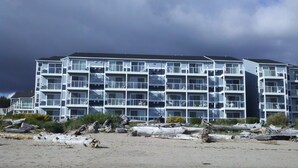 Un hôtel à plusieurs étages, doté de balcons, situé près d’une plage où l’on trouve du bois flotté.