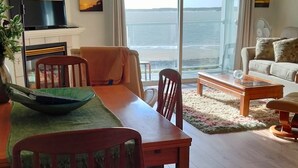 Un salon comprenant une table à manger, des chaises, un canapé et offrant une vue sur la mer grâce à de grandes fenêtres.
