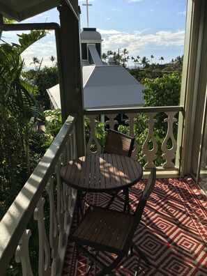 A balcony with a table and chairs, a patterned rug, and a view of a church and palm trees.
