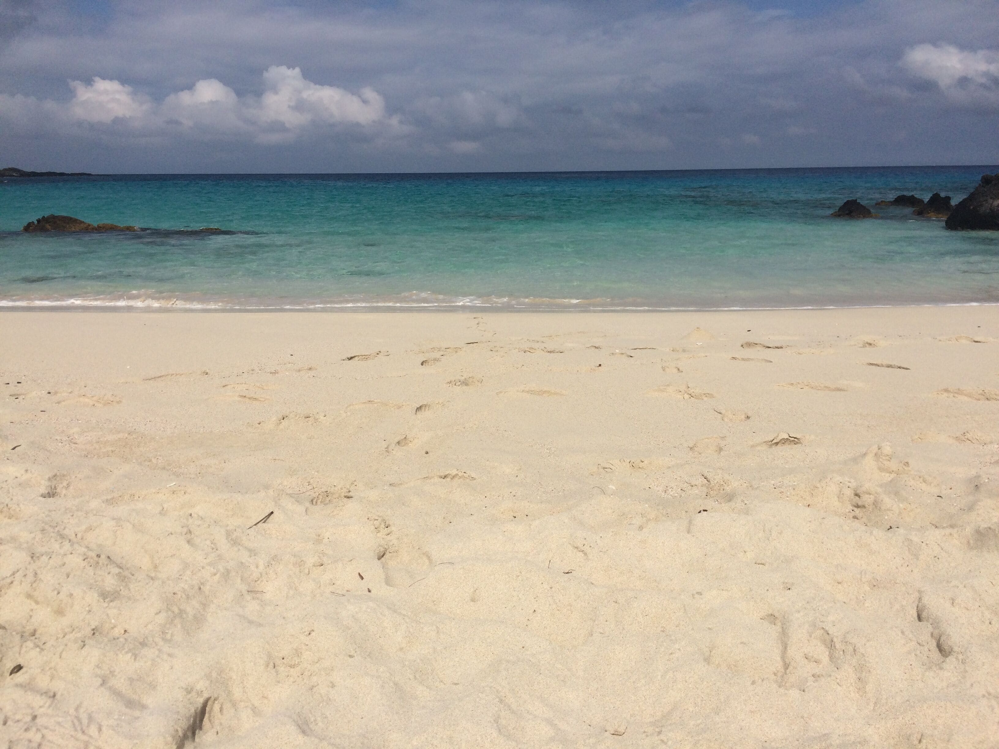 A beach with footprints in the sand and a calm sea.