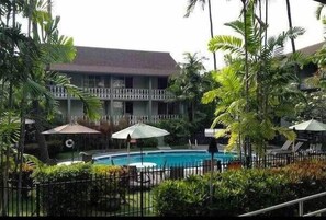 A hotel with a swimming pool surrounded by lush greenery and palm trees.