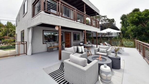 A modern two-story house with a balcony, outdoor seating area, and a fire pit.