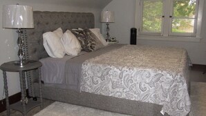 A bedroom with a large bed, two bedside tables, a window with blinds, and a carpeted floor.