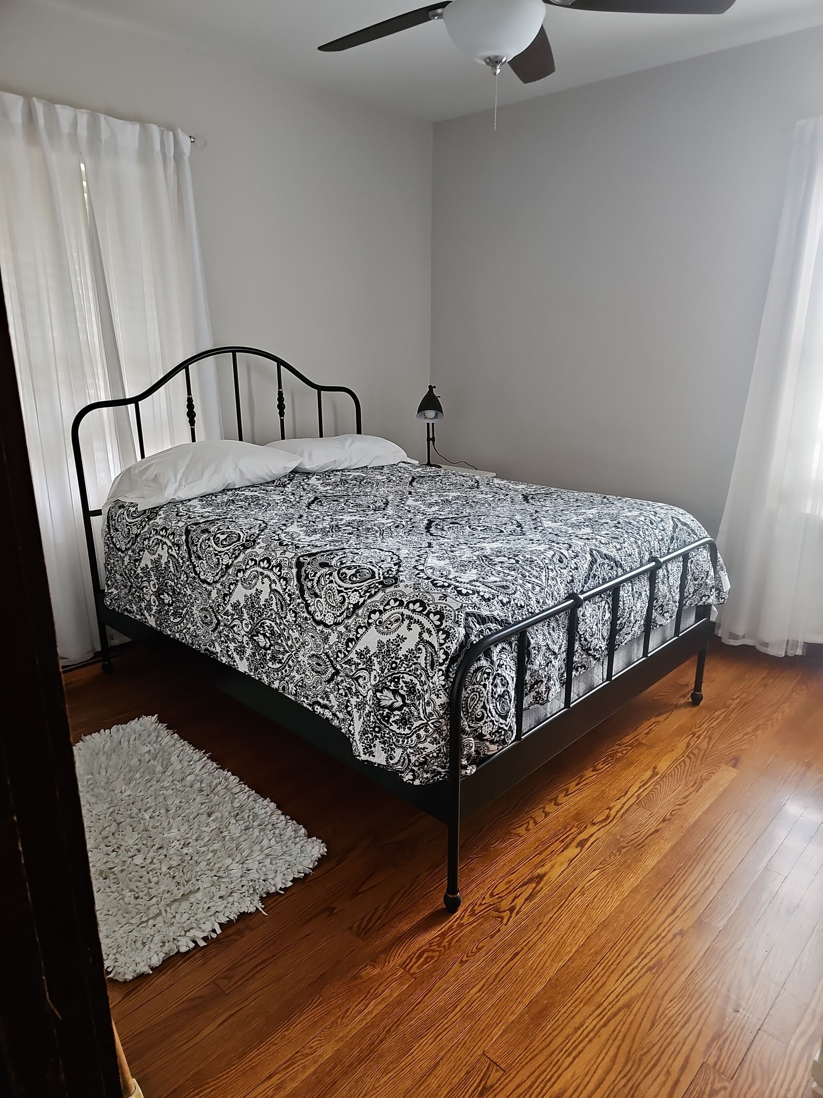 Une chambre à coucher avec un lit, un ventilateur de plafond, une lampe de chevet et un tapis blanc.