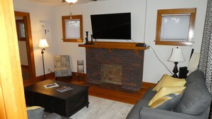 Una sala de estar con chimenea, un televisor montado encima, un sofá, un sillón y una mesa de centro.