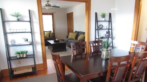 A dining area with a wooden table and chairs, surrounded by black shelves with plants and decorative items.
