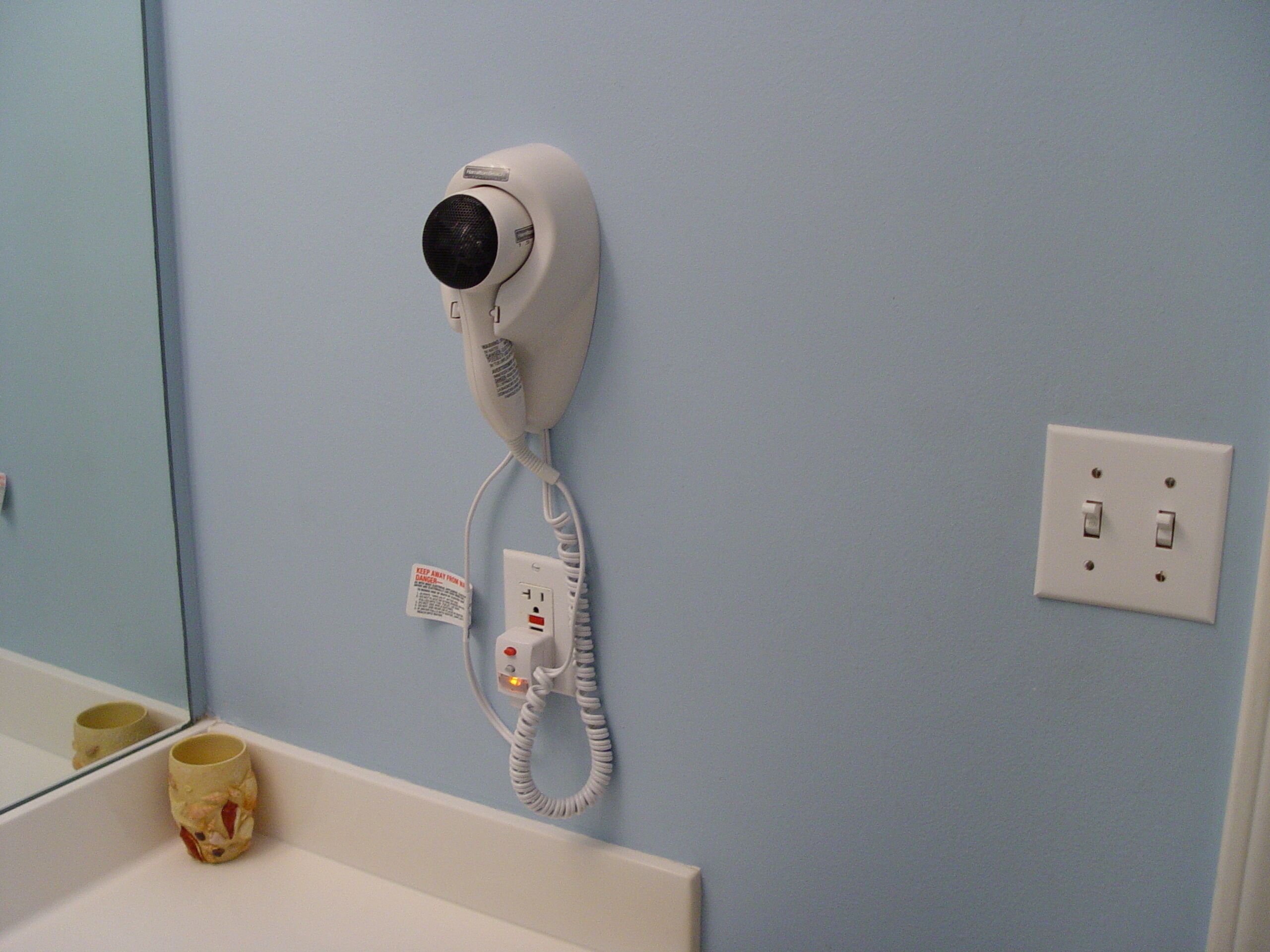 A hair dryer mounted on a wall with a power outlet and a switch.