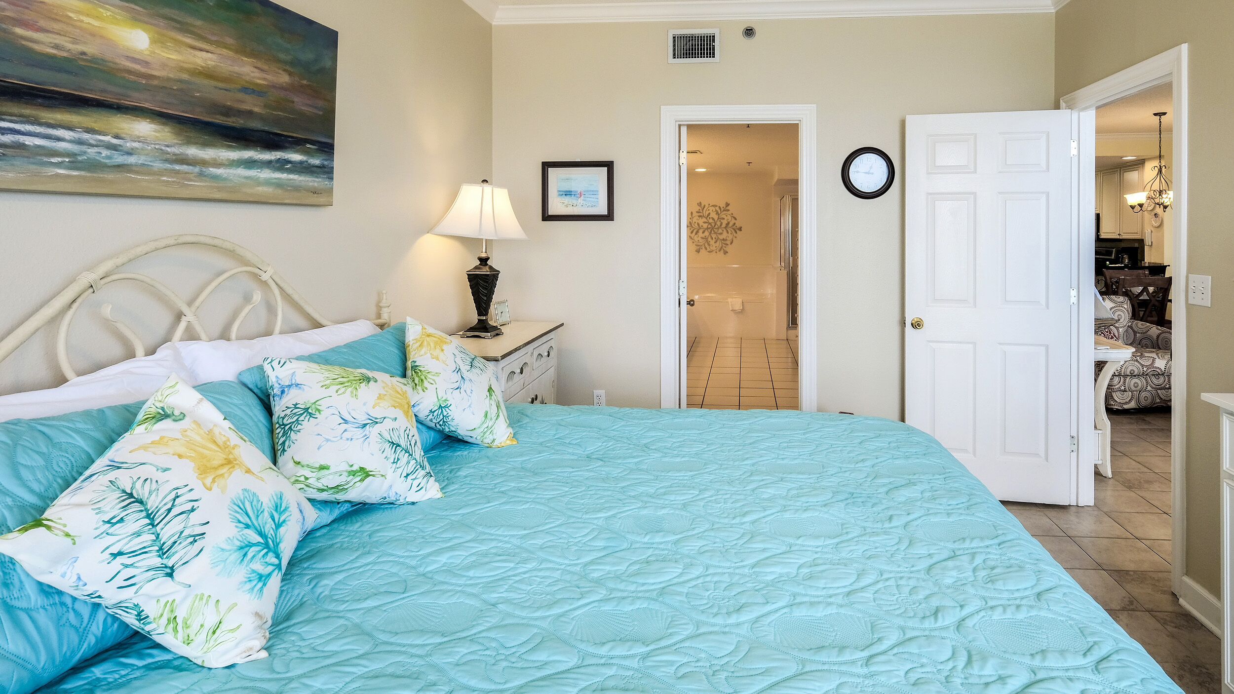 A bedroom with a bed, a nightstand, a lamp, a painting, and a door leading to another room.