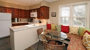 A compact kitchen with wooden cabinets, a built-in microwave, and a dining area with a glass table and wicker chairs. - Culp House: Ideal Location, Historic Gettysburg! Can Rent with the Cricket House (Gettysburg)