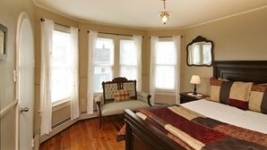 A bedroom with a large bed, a nightstand, a chair, and a window with curtains. - Culp House: Ideal Location, Historic Gettysburg! Can Rent with the Cricket House (Gettysburg)