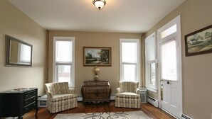 A room with a wooden floor, a patterned rug, a dresser, two upholstered chairs, a painting on the wall, and a door with a window. - Culp House: Ideal Location, Historic Gettysburg! Can Rent with the Cricket House (Gettysburg)