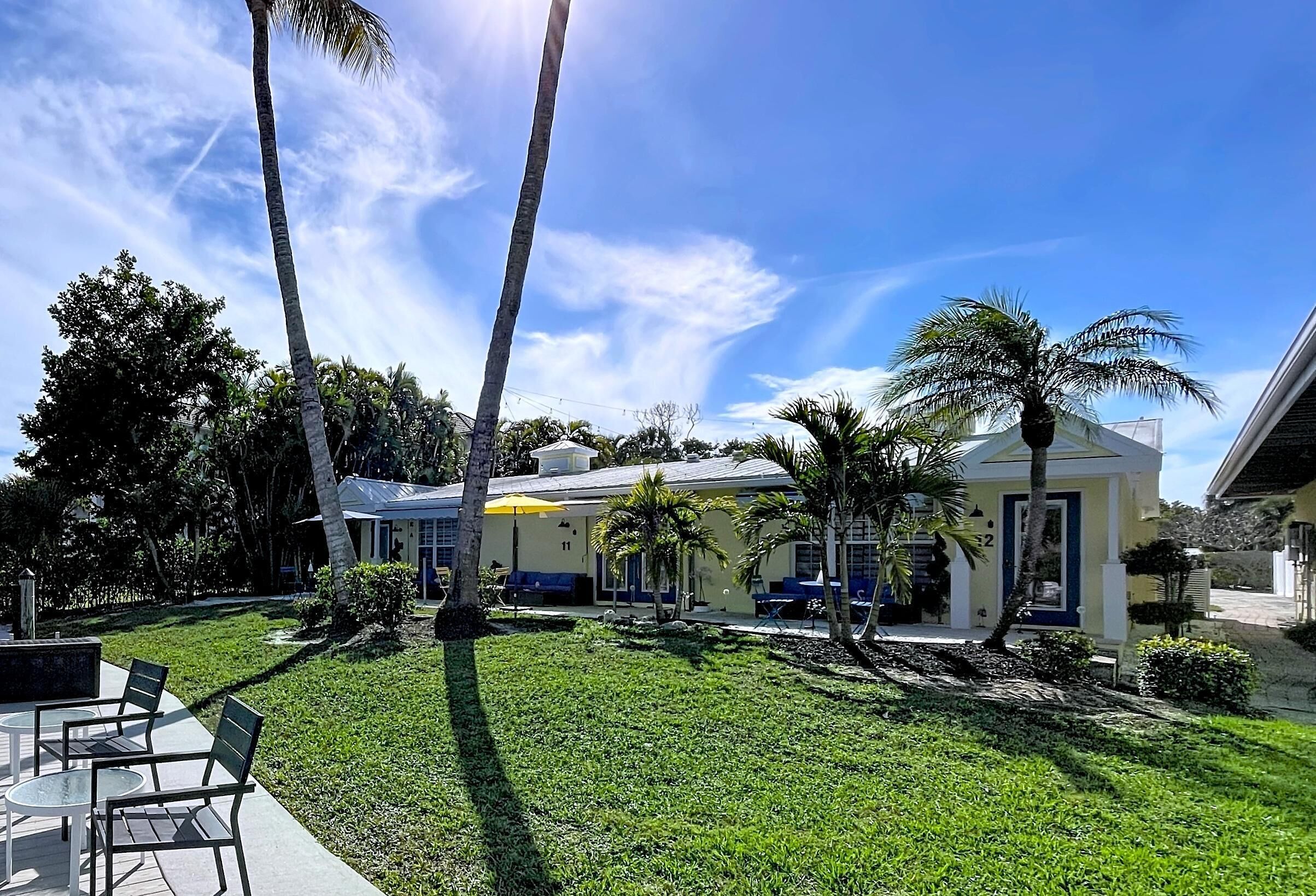 A residential property with a well-maintained lawn, palm trees, and a house with a yellow facade and blue accents.