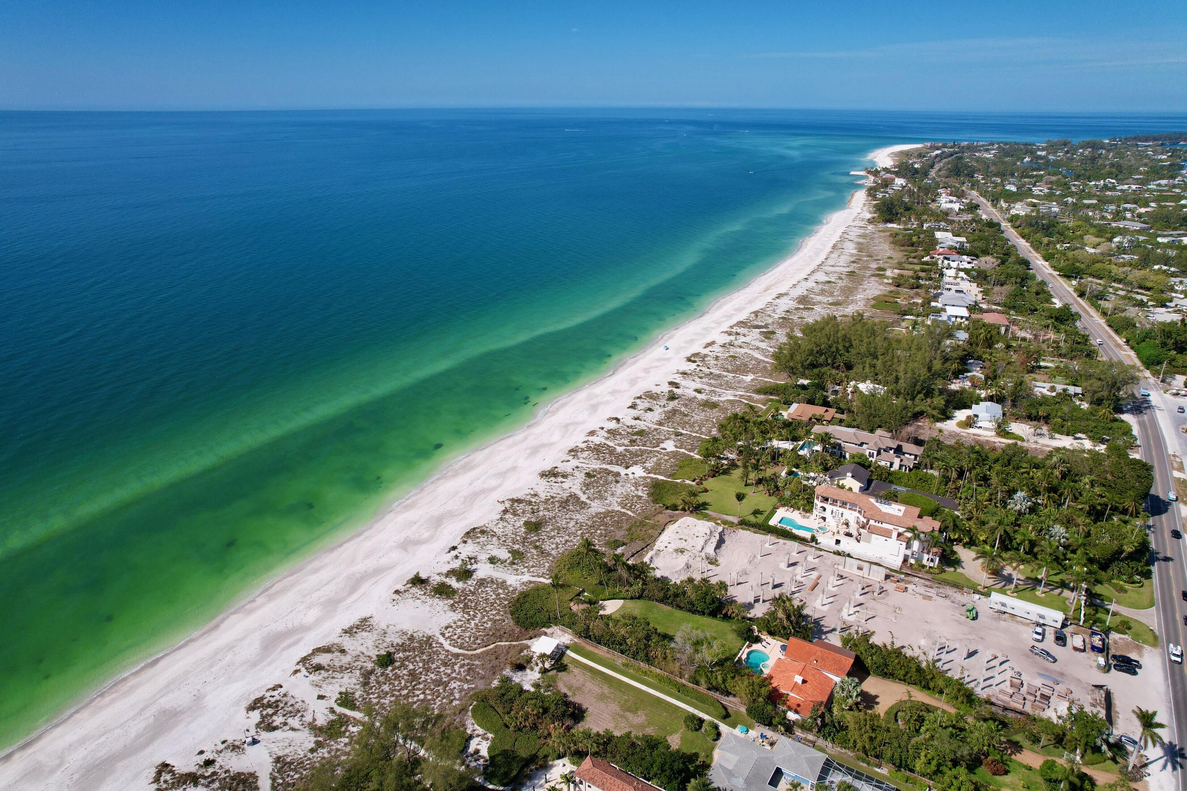 An aerial view of a coastal area with a beach, residential buildings, and a road.