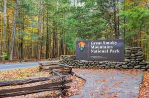 A sign for Great Smoky Mountains National Park with a stone wall and wooden fence.