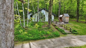 Een chalet met een houten trap naar een veranda, omringd door weelderige begroeiing en bomen.