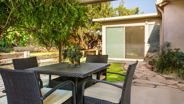 A patio with wicker furniture, a table with a vase, and a view of a house with a sliding door. - Outstanding Northeast Heights Home Near Casino/Golf/Breweries/Hiking/Dog Park (Albuquerque)