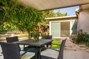 A patio with wicker furniture, a table with a vase, and a view of a house with a sliding door. - Outstanding Northeast Heights Home Near Casino/Golf/Breweries/Hiking/Dog Park (Albuquerque)