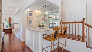 Un pasillo amplio con escaleras de madera, una vitrina de cristal con objetos decorativos y sillas de mimbre.